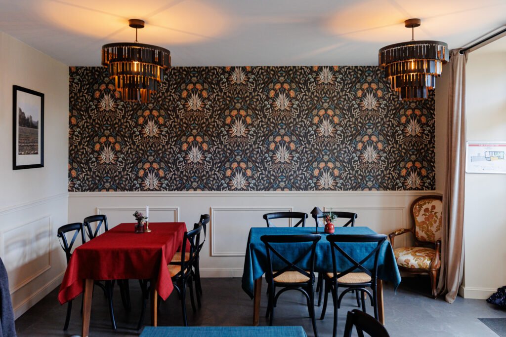 Interior of the Salicorne restaurant with set tables, red and blue tablecloths, and floral wallpaper.