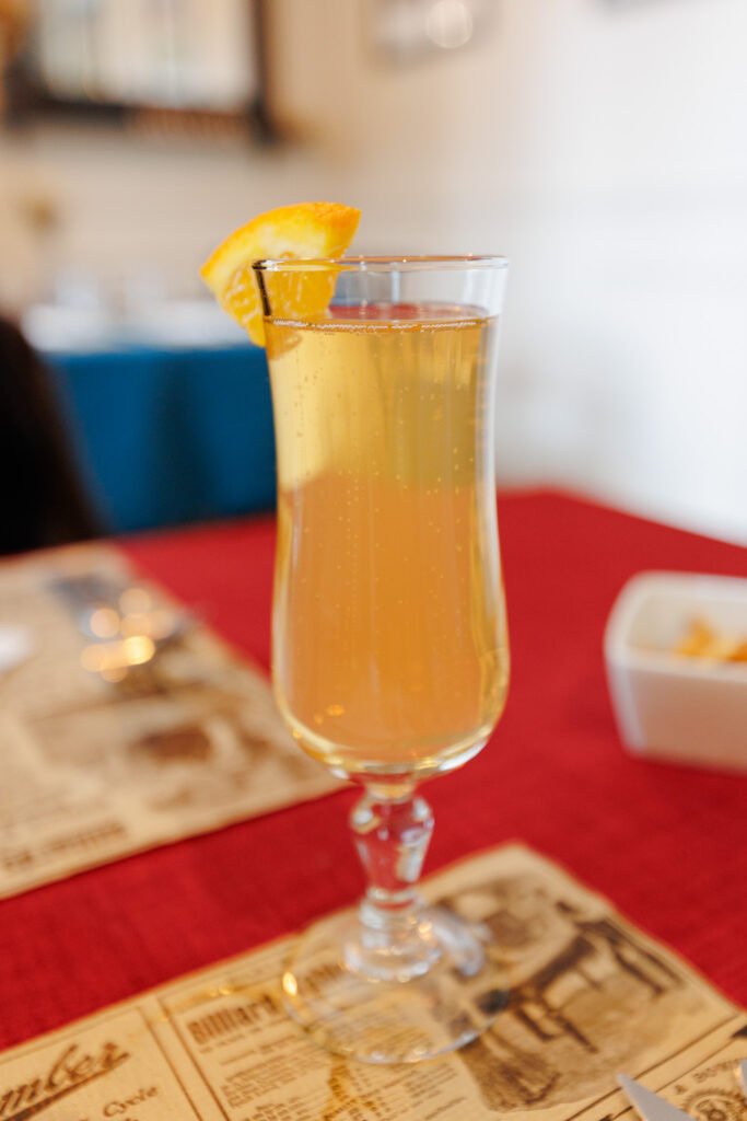 Glass of sparkling cocktail garnished with an orange slice placed on a set table.