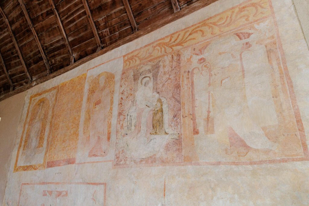 Ancient and faded wall paintings on a wall beneath a wooden framework in Saulges