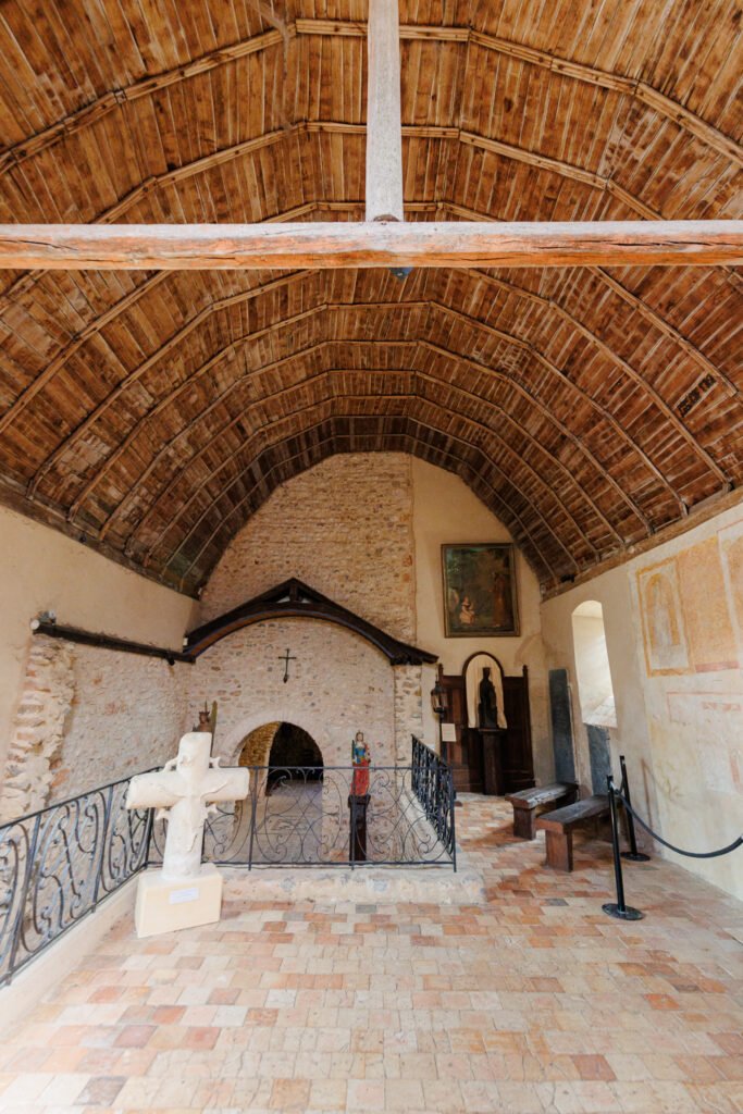 Interior of the Romanesque church of Saulges with its exposed wooden framework and a carved cross.