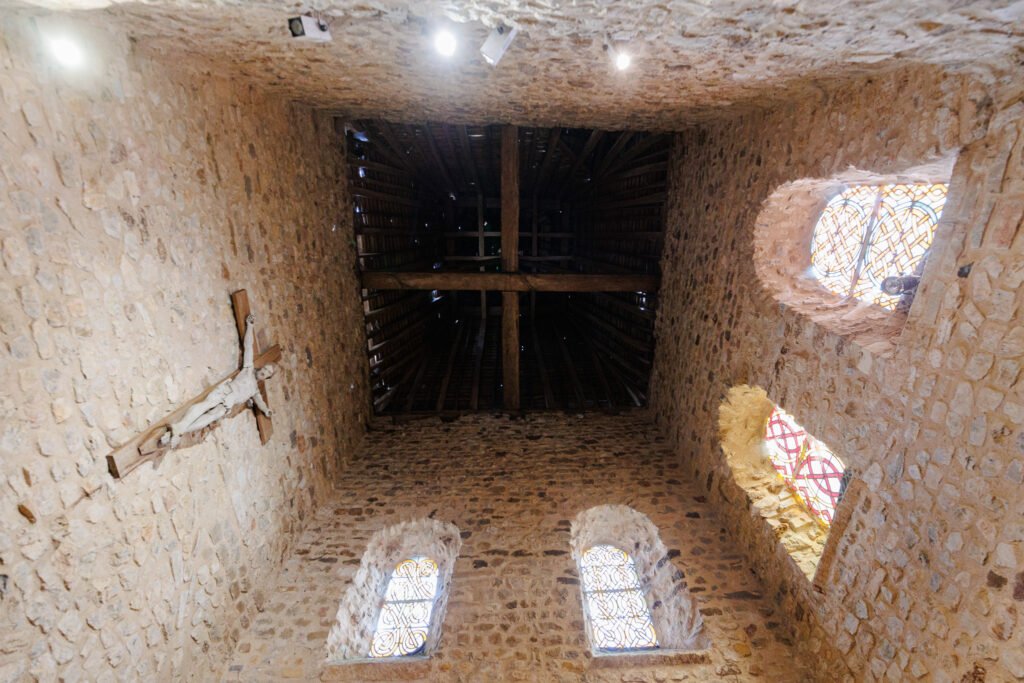 Interior of the Saulges church showing the wooden framework, stone walls, and stained glass windows.