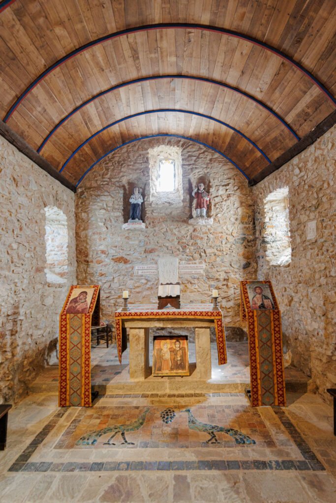 Interior of the Saulges oratory with its stone altar, religious icons, and exposed stone walls.