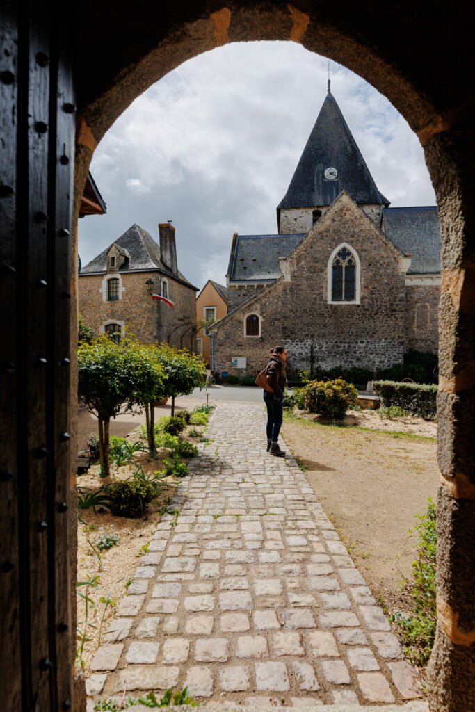Cobbled alley leading to a stone church in the historic village of Saulges, framed by a stone porch.