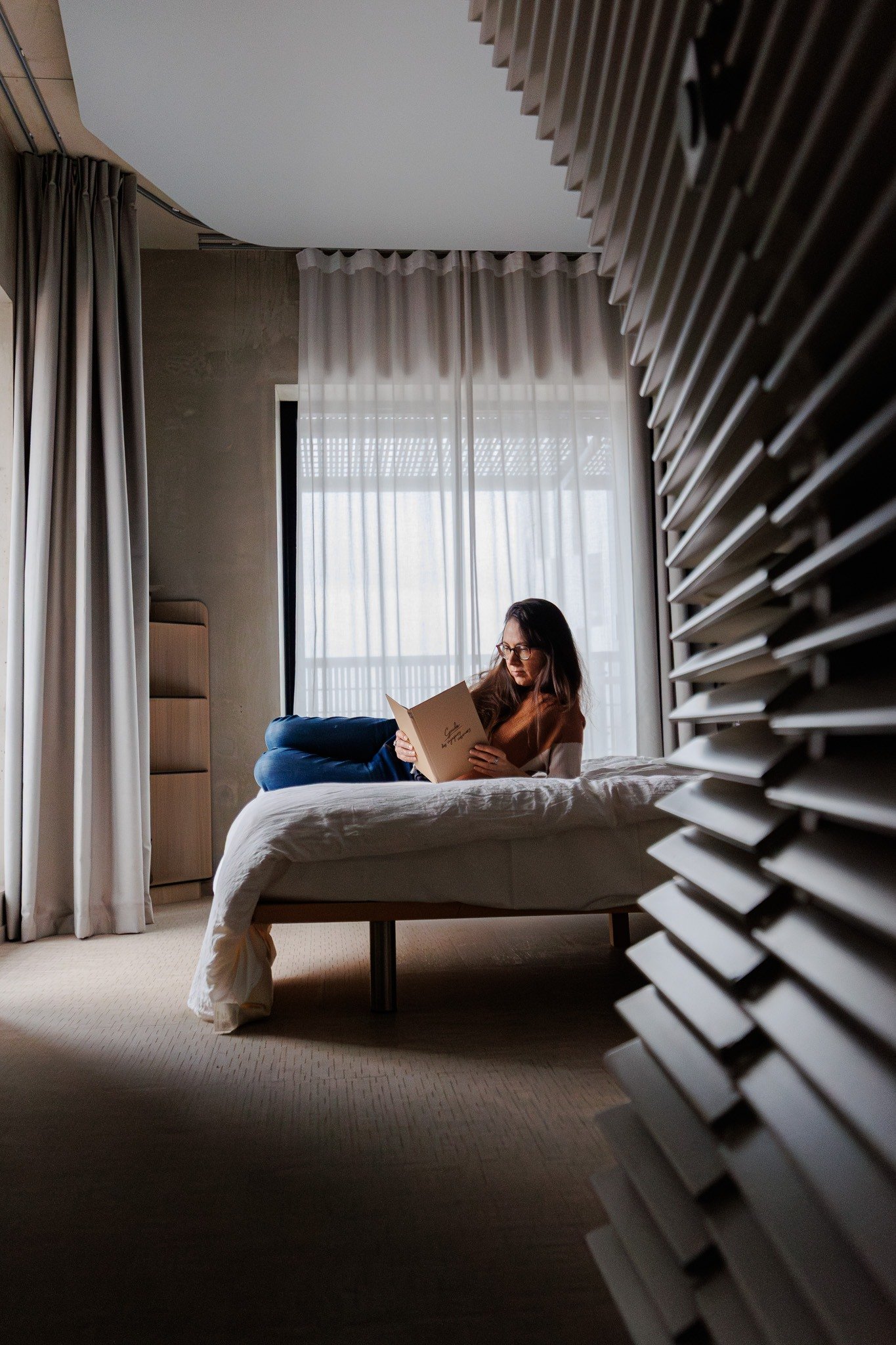 Gaëlle lit près de la fenêtre d’une chambre à OKKO Hotels Strasbourg.