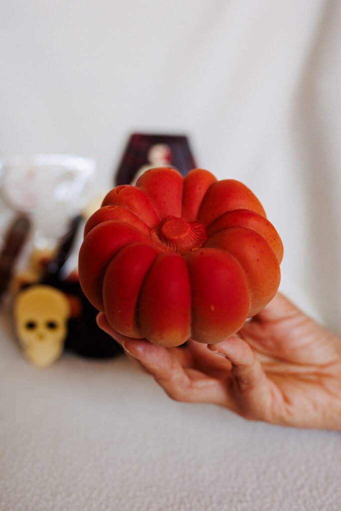Main tenant une citrouille pâtissière rouge pour Halloween à Paris avec des décorations floues en arrière-plan.